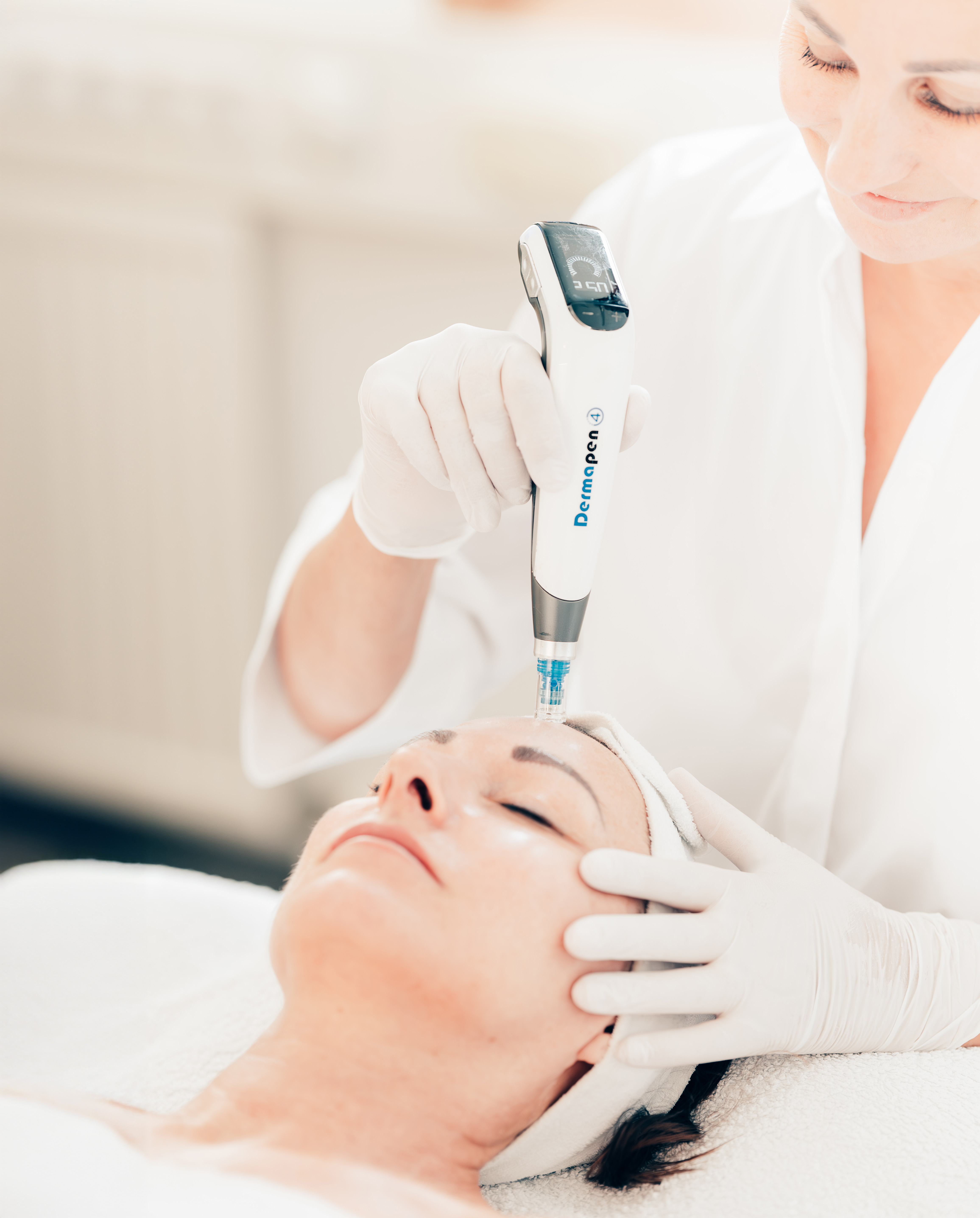 Kosmetikerin führt mit einem Dermapen eine präzise Microneedling-Behandlung auf der Stirn einer entspannten Kundin durch.