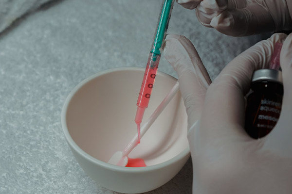 Kosmetikerin füllt rosa Wirkstoff aus Spritze in eine Schale – Vorbereitung für eine ästhetische oder medizinische Hautbehandlung.